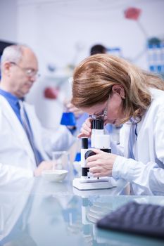 Senior female scientist doing medical research looking at sample under a microscope. Phermaceutical research in a laboratory.