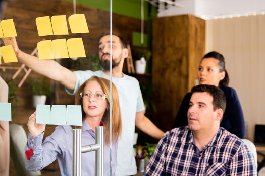 Group of young entrepreneurs looking at sticky notes on a glass window in modern office