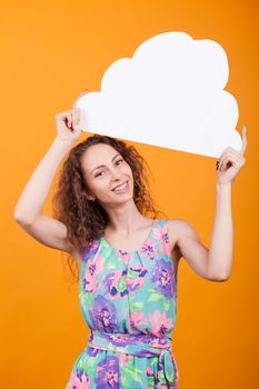 Funny woman holding a bubble thought sign over head in studio with orange background. Caucasian woman smiling.