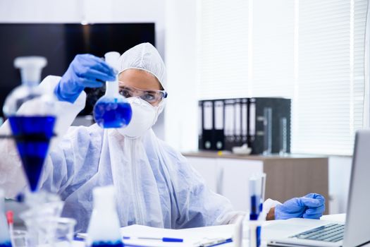 Scientist looks at a tube with a blue liquid from which a white smoke comes out