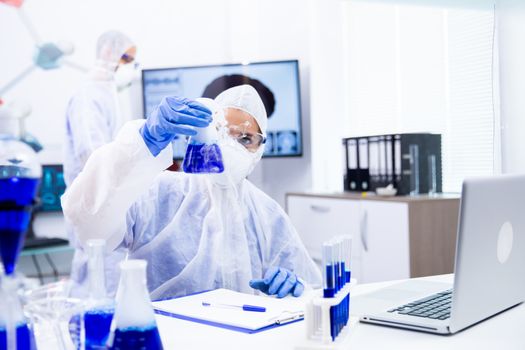 Chemist holding a container of blue liquid from which comes a white smoke.