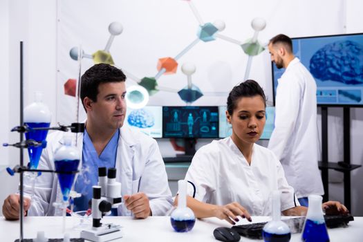 Female scientist in white coat typing on cumputer. Modern microscope.