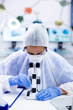 Female chemist in gloves and goggles adjusts microscope. Pharmaceutical research