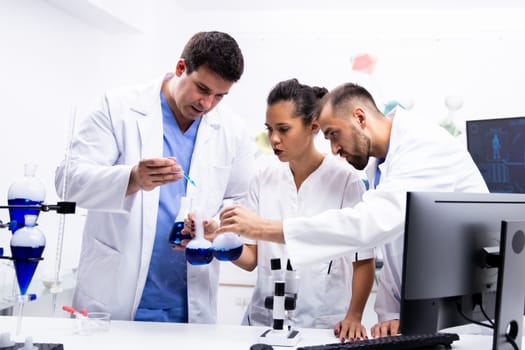 Team of scientist in white coat working together with smoking blue liquid in modern research lab.