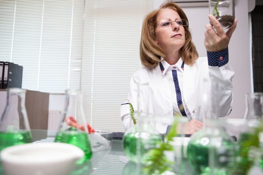 Female scientist doing alterniative research on plants. Female scientist in white coat. Test tubes.
