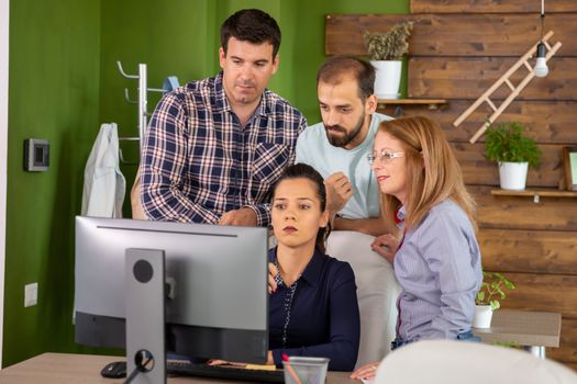 Team gathered behind their manager looking into computer monitor. Young manager.