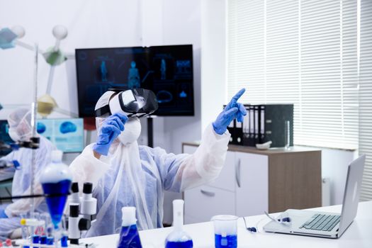 Female scientist wearing virtual reality goggles to simulate research test in modern chemistry laboratory.