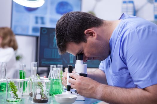 Young scientist man doing a quality control looking through microscope in a research lab. Biologist in research lab.