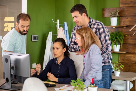 Team of people in start-up office talking at a colleague desk. Working in professional creative environment