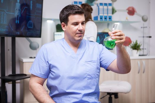 Portrait of microbiologist man holding a test tube with green solution in scientific laboratory. Genetic test.