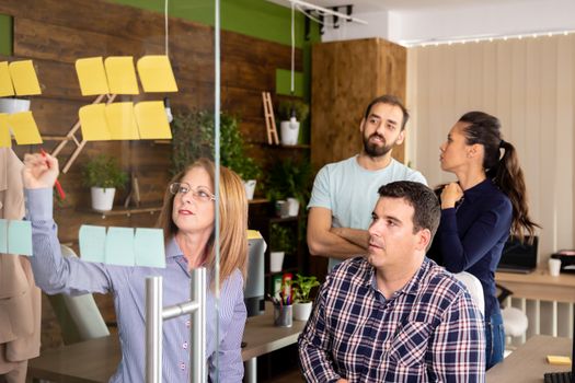 Team of four office workers looking at glass window full with stickers. Cozy start up office company