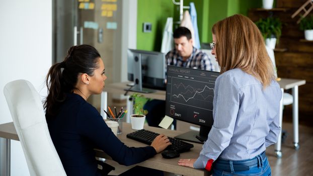 Two businesswomen discuss the graphs in the report. Comfortable office