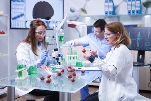 Caucasian woman with protection glasses doing scientific test on strawberries. Processing strawberries.