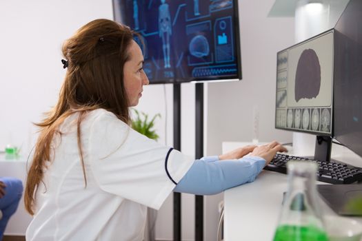 Portrait of mature biologist woman working on computer. Modern equipment in a microbiological laboratory.