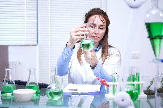Female scientist looking with great attention on a green solution. Research lab.