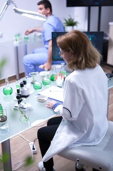 Middle age female scientist taking a sample of soil for for microscope analysis. Young biologist working in the background.