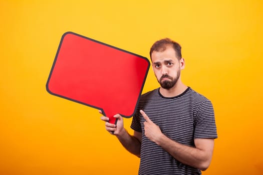 Portrait of sad young man pointing at his informing sign over yellow background. Handsome man.