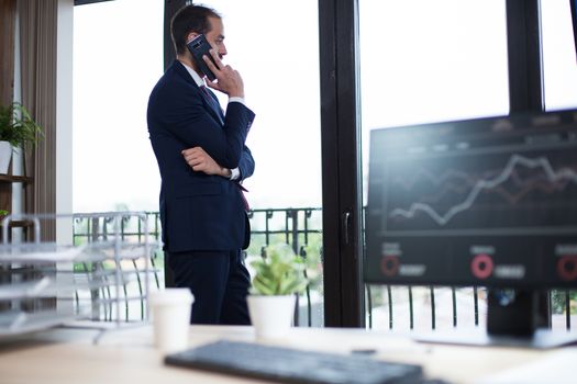 Young businessman looking out of window from his office and talking on the phone. Serious businessman.