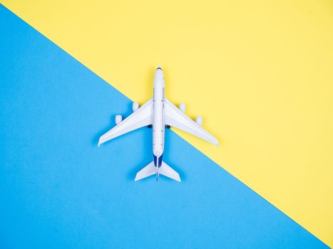 Top view of white toy plane over yellow and blue background. Copyspace available.