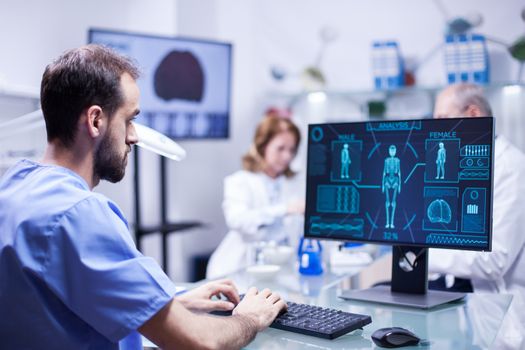 Young technician typing data for human body neurology system in science laboratory. Specialist working.