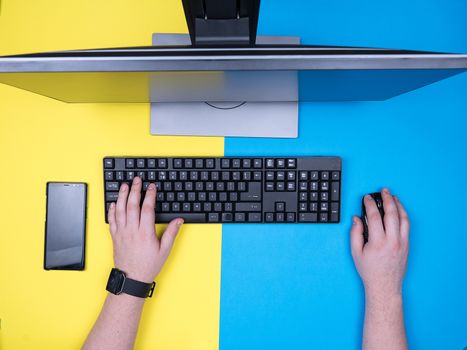 Flat lay top of man typing on a computer keyboard over blue and yellow background. Modern computer for business. Modern technology.