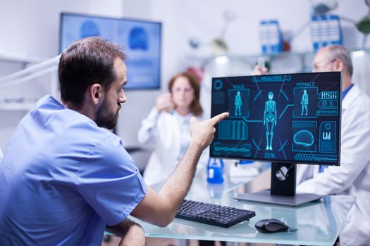 Young engineer in inovation center for body research pointing at monitor. Team of scientists in a innovation center.