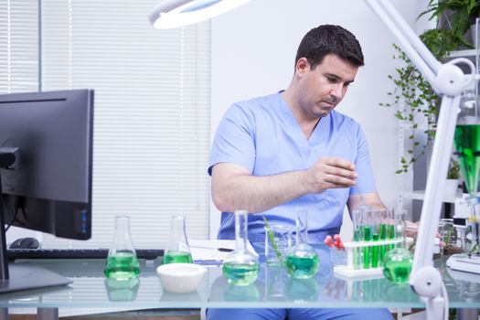 Young caucasian scientist man taking a sample of solution from a test tube. Microbiology lab.