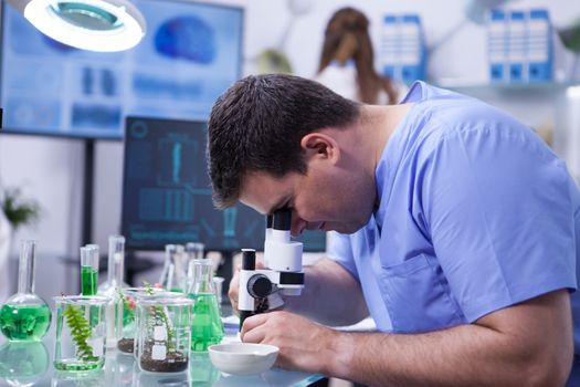 Caucasian scientist man in a biotechnology lab Looking through microscope. Female scientist in the background.
