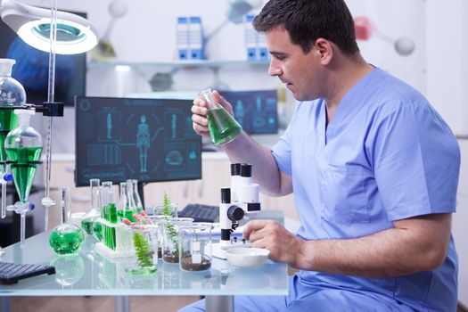 Side view of young scientific man holding a green solution in his research lab. Chemistry lab.