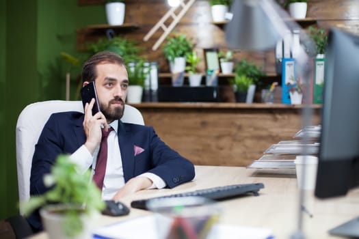 Young and elegant businessman checking the data from his monitor and having a business conversation on his mobile phone. Smart businessman.