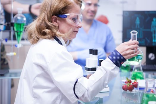 Side view of female scientist holding a test tube with green solution. Research lab.