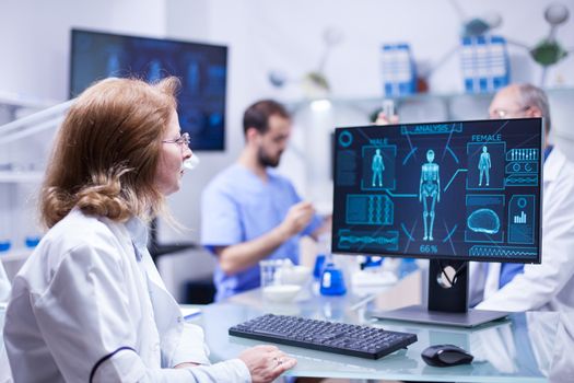 Female scientist looking at the monitor screen in research room. Chief of development working with test tubes in the background.