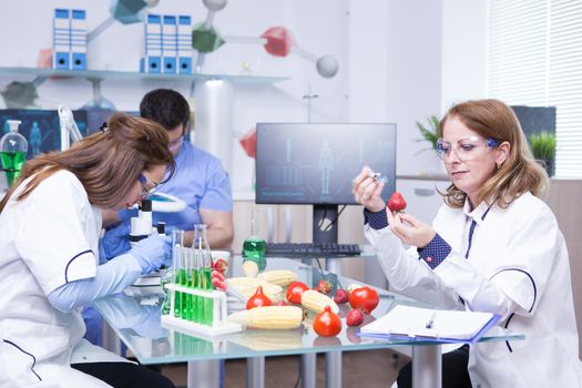 Treatment study on genetically engineered strawberries in laboratory by group of scientist. Test tubes with green solutions.