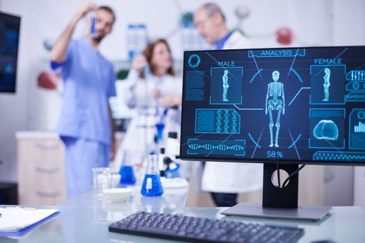 Display monitor in a hospital laboratory showing human skeleton. Team of scientist working in the background.