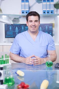 Portrait of male scientist in lab research wearing his uniform and smiling to the camera. Test tubes with green solutions.
