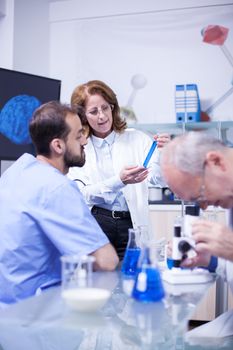 Medical professor working with microscope in the hospital laboratory. Chemist working with dangerous liquids in the background.