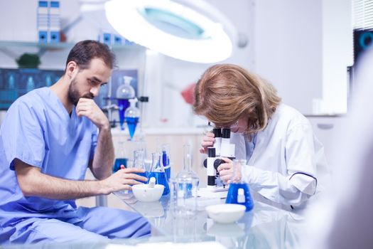 Middle age female scientist working with microscope in laboratory. Young caucasian male working as technician in a research laboratory.