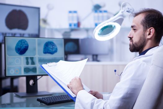 Portrait of young doctor checking his clipboard notes for his next surgery. Doctor looking at brain x-ray.