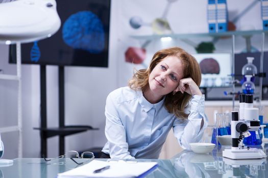 Middle age woman with red hair in a biomedical laboratory. Monitor with brain image in the background.
