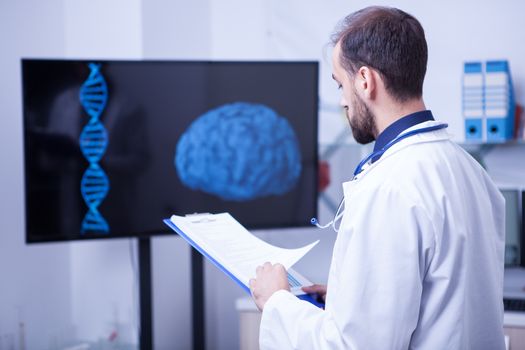 Specialist doctor in a laboratory looking at the scan of a brain holding a clipboard. Doctor with stethoscope around his neck.