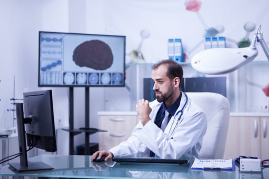 Side view portrait of young doctor with his hand on the mouse and checking his consultations for the day. Young medic practitioner.