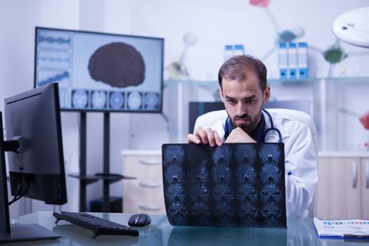 Handsome bearded doctor looking at a brain radiography. Doctor sitting at his desk in a cabinet checking a brain ct scan.
