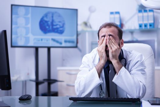 Portrait of young doctor rubbing his eyes wearing a white coat. Tired doctor in the hospital.
