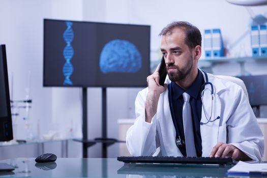 Doctor with white coat having a phone call at hospital cabinet. Doctor using modern technology.