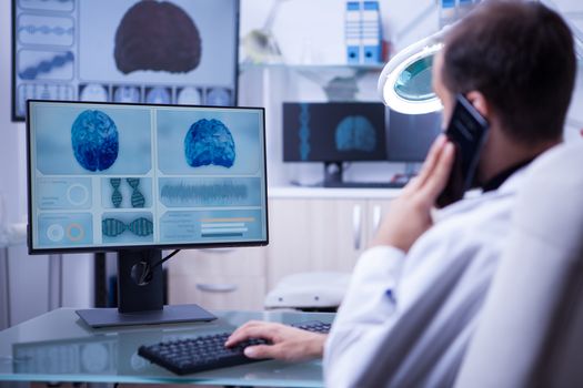 Male doctor using telephone while working on computer typing. Young doctor in a hospital office.