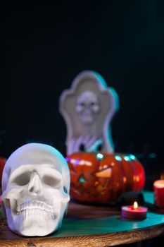 Creepy human skull with other halloween decorations on a wooden table. Halloween celebration.