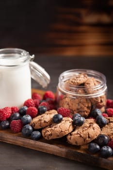 Delicious oatmeal cookies with fresh raspberries and milk over rustic wooden table. Tasty bakery.