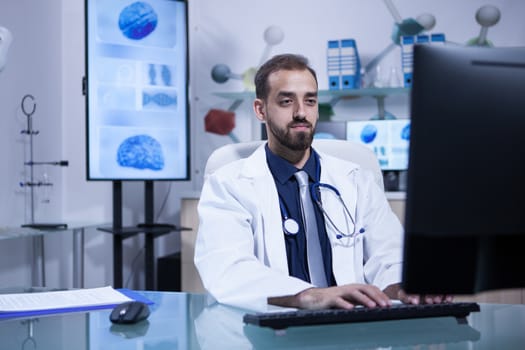 Motivated handsome young doctor working on his computer in the hospital office. Specialist doctor.