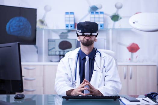 Portrait of doctor sitting at his desk using virtual reality headest looking up. Doctor using modern techology.