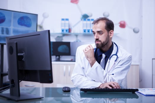 Focused young and handsome doctor on his daily work at the clinic. Portrait of doctor in his cabinet.